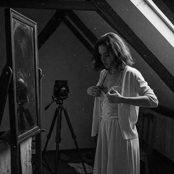 Public exposure erotica image of a submissive woman undressing in front of a mirror with a vintage camera watching, CMNF, ENF, shame kink, voyeuristic stillness.