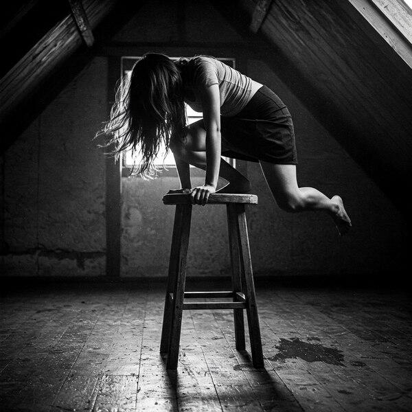 Erotic humiliation photo of a submissive woman climbing a wooden stool in an attic, caught mid-motion with hair falling forward, CMNF, ritual exposure, orgasm control, shame kink.